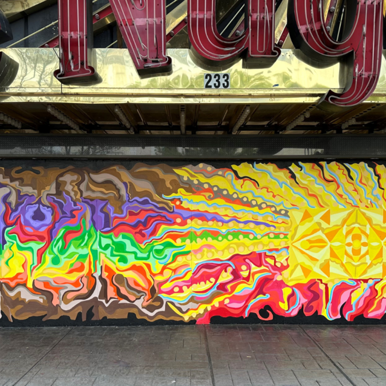 Mural painted under the sign, "The Nugget" with red, orange, yellow, green, and purple abstract shapes and lines.