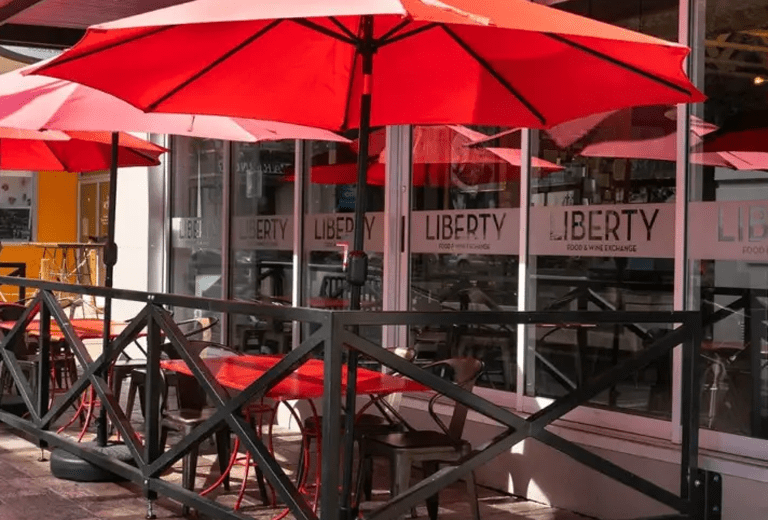 Exterior patio of Libery Food and Winte. There are red umbrellas and a black fence.