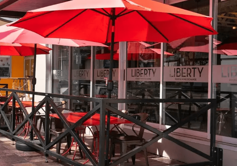 Exterior patio of Libery Food and Winte. There are red umbrellas and a black fence.