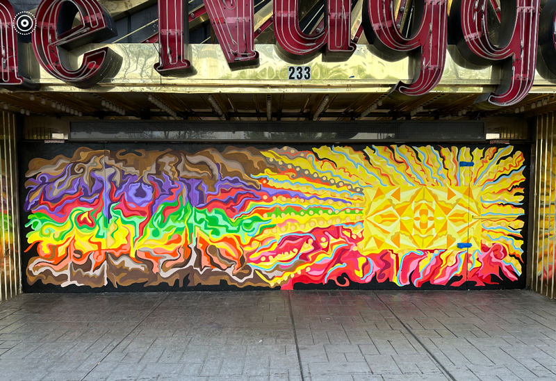 Mural painted under the sign, "The Nugget" with red, orange, yellow, green, and purple abstract shapes and lines.