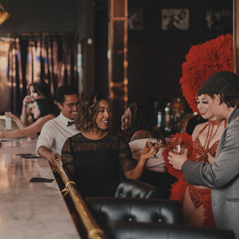 People smiling and cheersing with cocktails in hand at a speakeasy bar.