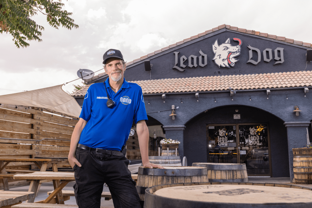 A downtown Reno ambassador poses with his left arm leaning on a barrel. He is in front of Lead Dog Brewery found in Reno's Brewery District. The sky is slightly overcast but he seems hopeful for the day.